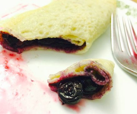 Gluten-free crepe with blueberries inside on plate, one bite cut off.