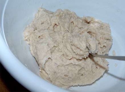 Gluten-free yeast bread dough in white mixing bowl with spoon stuck in it.