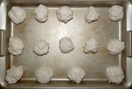 Baking tray with 14 balls of gluten-free yeast dough for rolls.