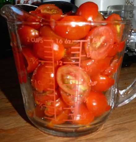 Two-cup glass measuring cup filled to brim with grape tomato halves.