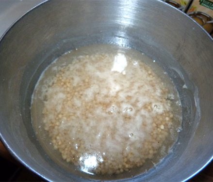 Uncooked whole grain sorghum covered with water in a metal bowl.