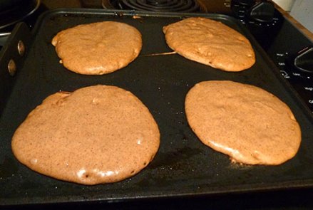Four gingerbread pancakes cooking on a griddle.